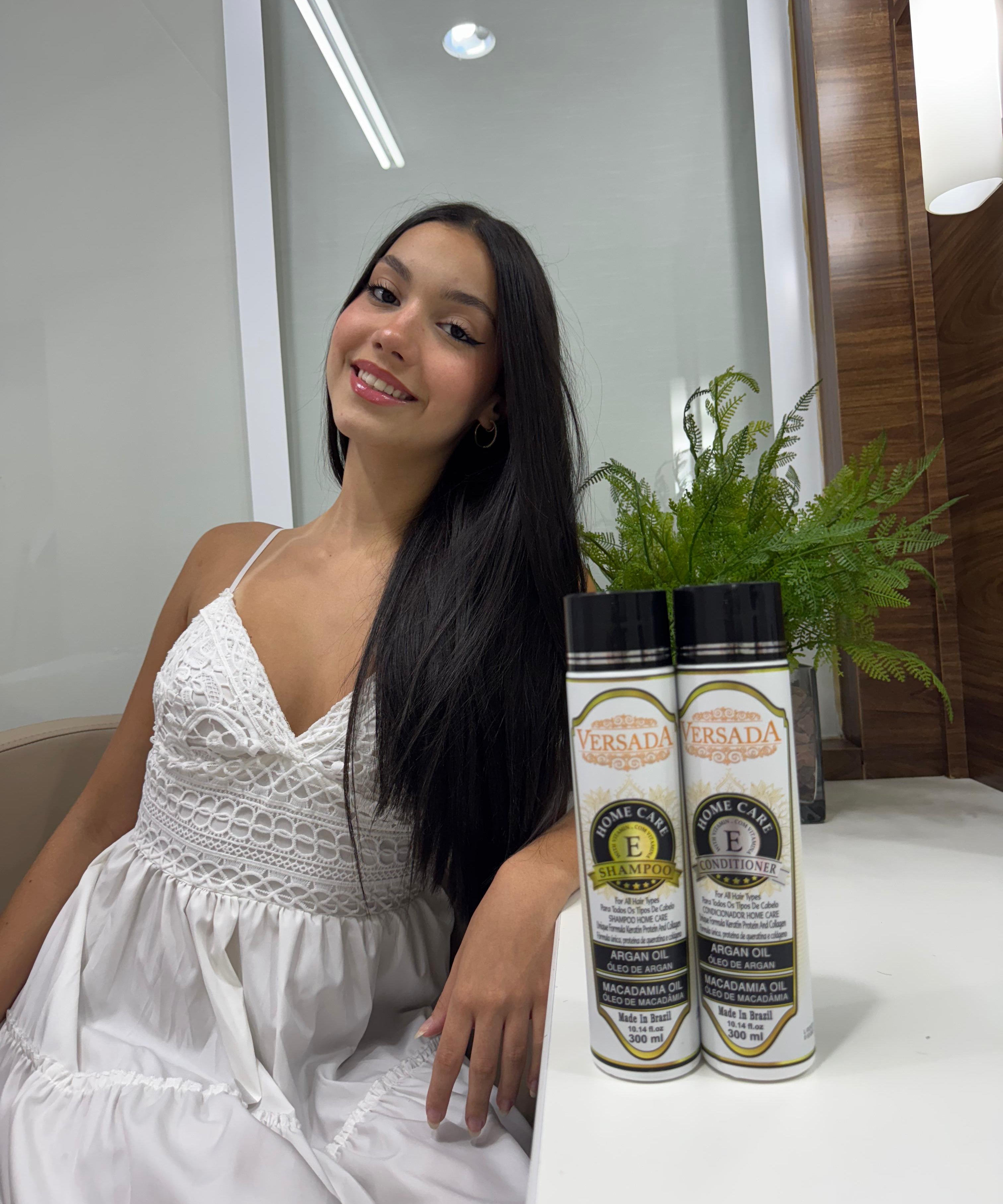 Woman in a white dress sitting next to two bottles of Versada hair care products.